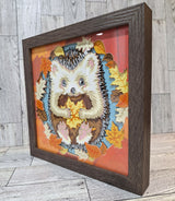 side view of framed hedgehog holding a fall leaf